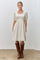 woman wearing a cream short puff sleeve dress with a square neckline and holding brown knee-high boots