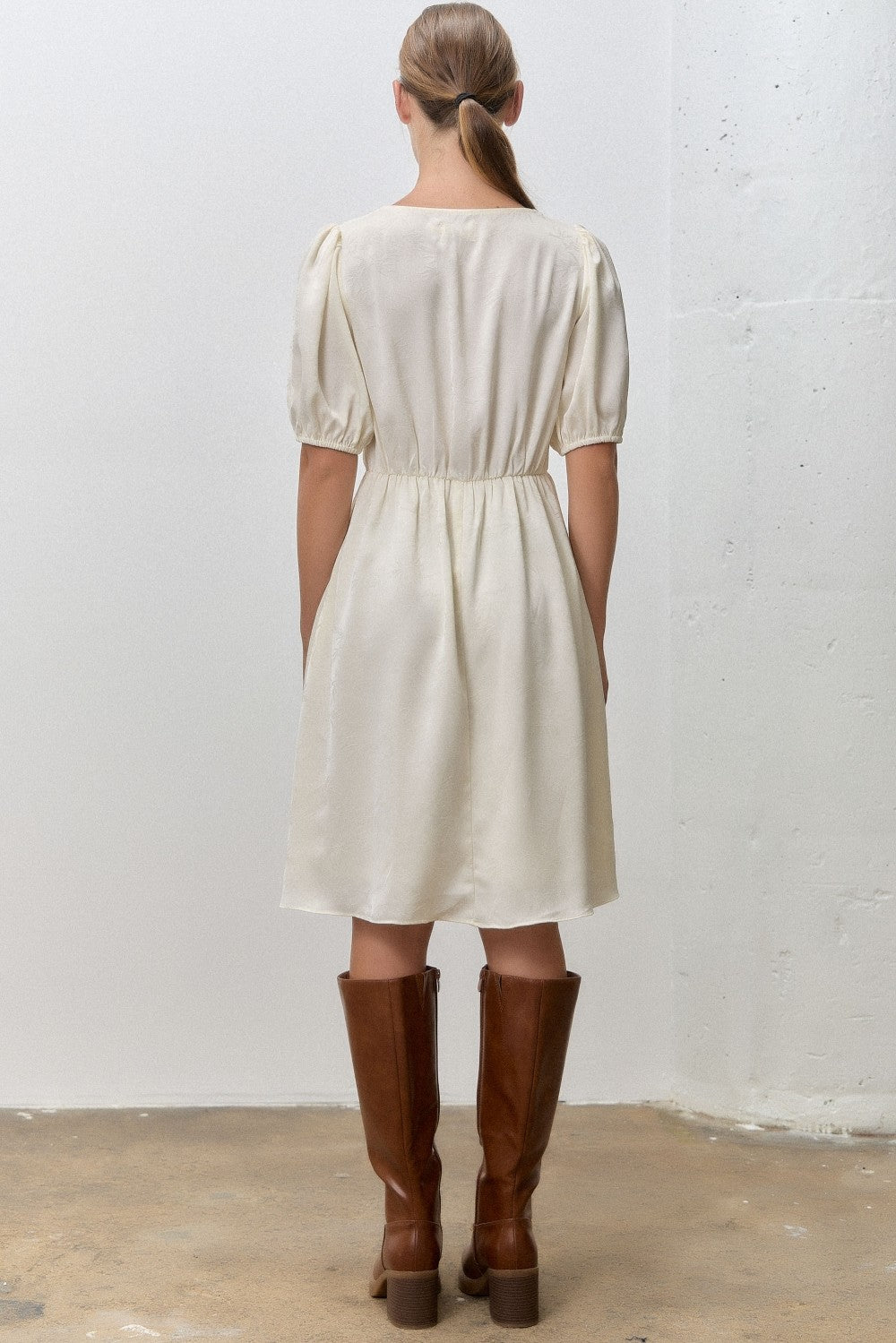 woman wearing a cream-colored short puff sleeve dress with a cinched waist and knee-high brown leather boots