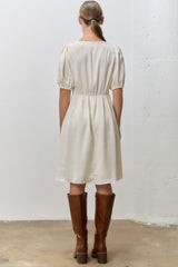 woman wearing a cream-colored short puff sleeve dress with a cinched waist and knee-high brown leather boots