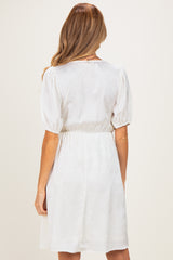 woman wearing a white short sleeve maternity dress with a fitted waist and puff sleeves, showing the back view