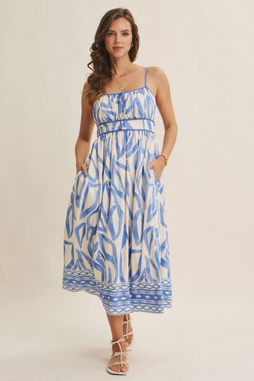 woman wearing a blue and white patterned midi dress with spaghetti straps and pockets, styled with strappy sandals