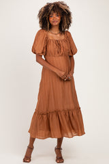 woman wearing a rust-colored maternity dress with balloon sleeves and a tiered hem, showing her baby bump