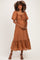 woman wearing a rust-colored maternity dress with balloon sleeves and a tiered hem, showing her baby bump