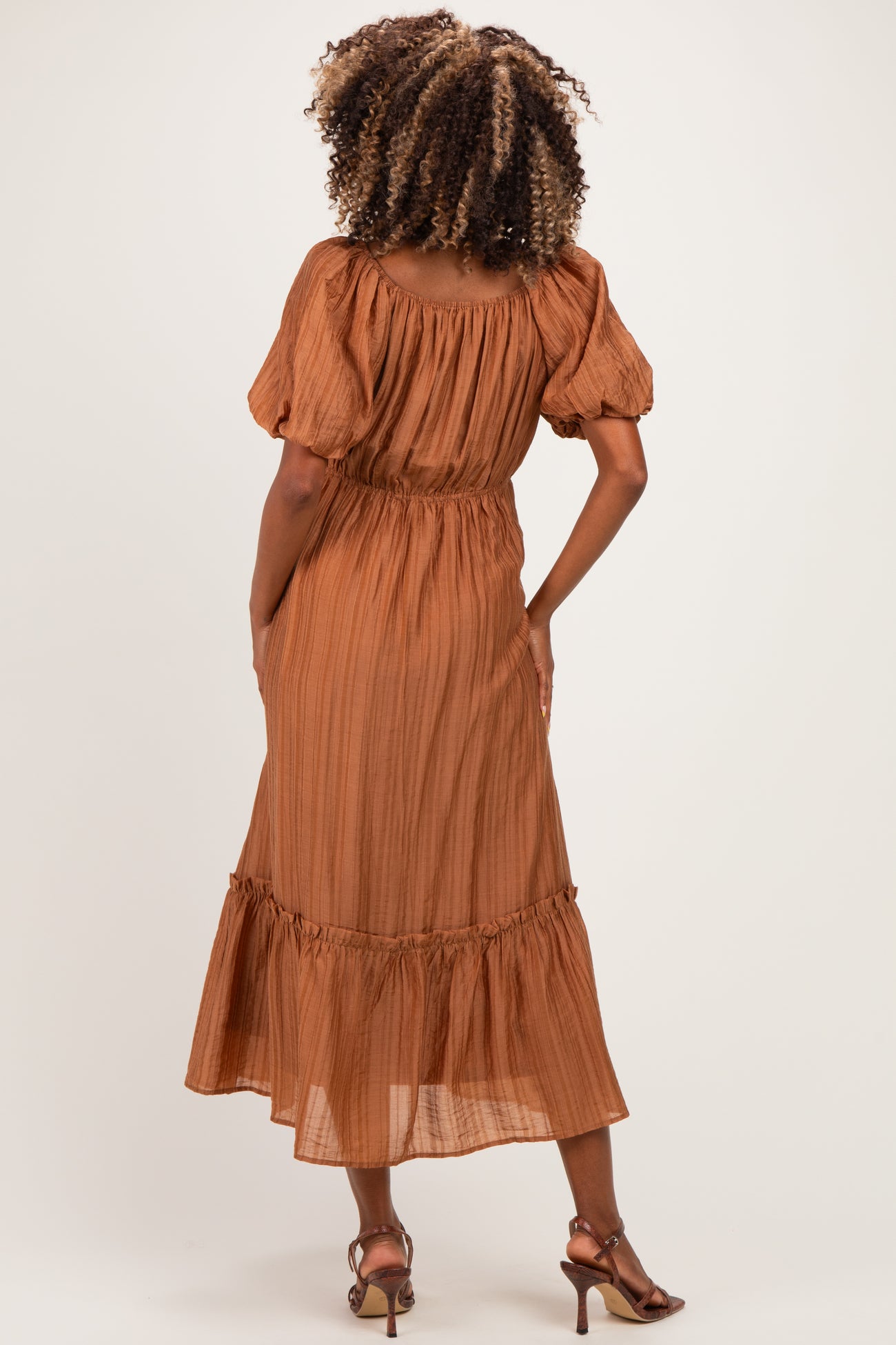 woman wearing a rust-colored maternity dress with puff sleeves and ruffled hem, showing her baby bump from the back