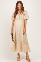 woman wearing a beige maternity dress with puff sleeves and ruffle hem, holding a clutch purse