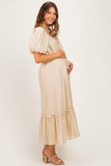 woman wearing a beige maternity dress with puff sleeves and a ruffled hem, cradling her baby bump