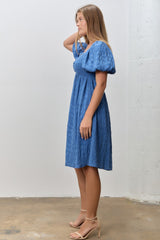 woman wearing a blue puff sleeve midi dress with a textured finish and an empire waist