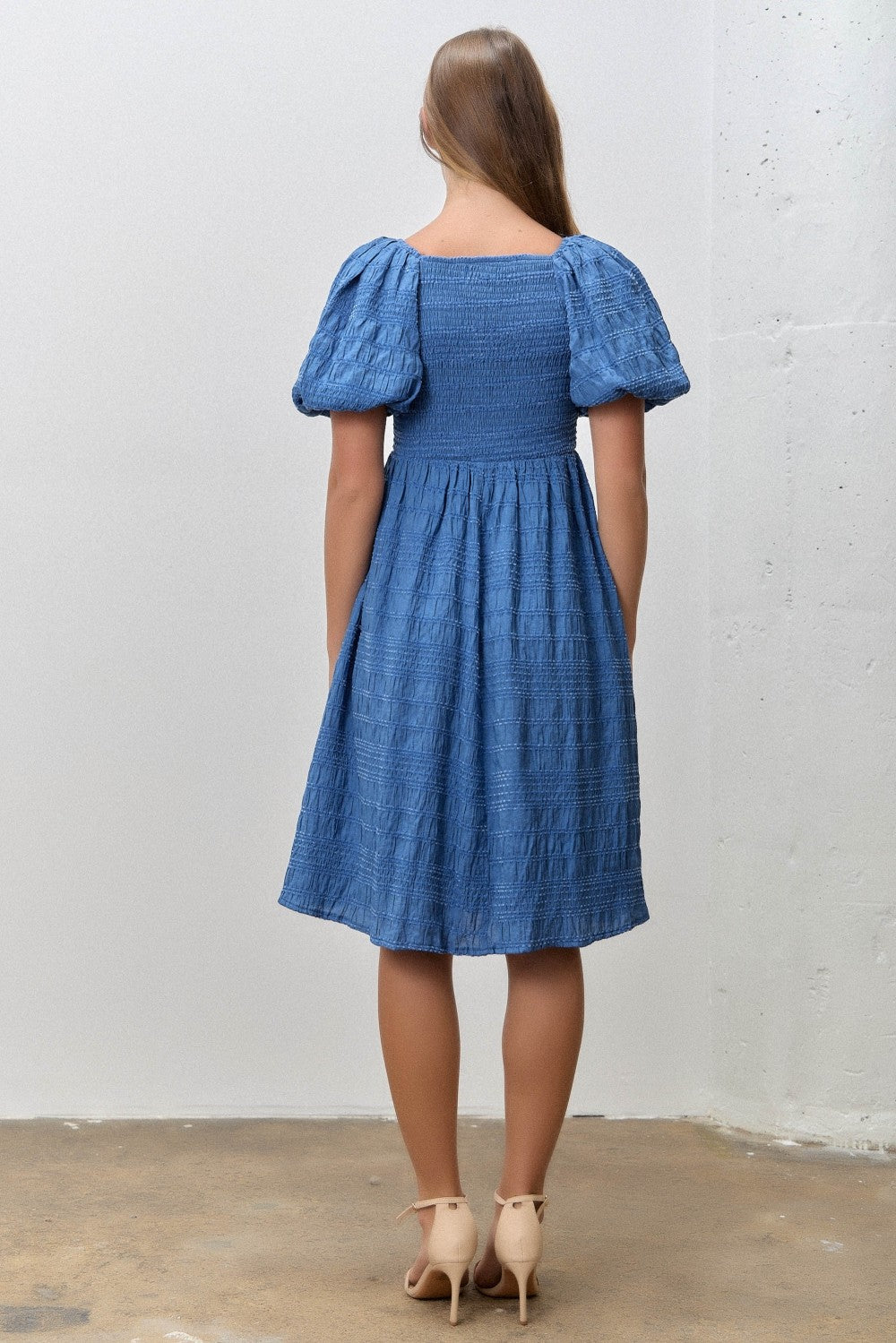 woman wearing a blue short puff sleeve dress with a smocked bodice and a flared skirt, seen from the back