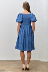 woman wearing a blue short puff sleeve dress with a smocked bodice and a flared skirt, seen from the back