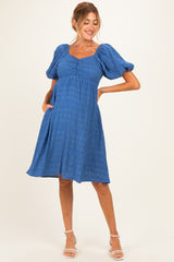 woman wearing a blue maternity dress with puff sleeves and a fitted bodice, showcasing her baby bump