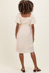 woman wearing a white short sleeve maternity dress with a floral print and gathered back detail