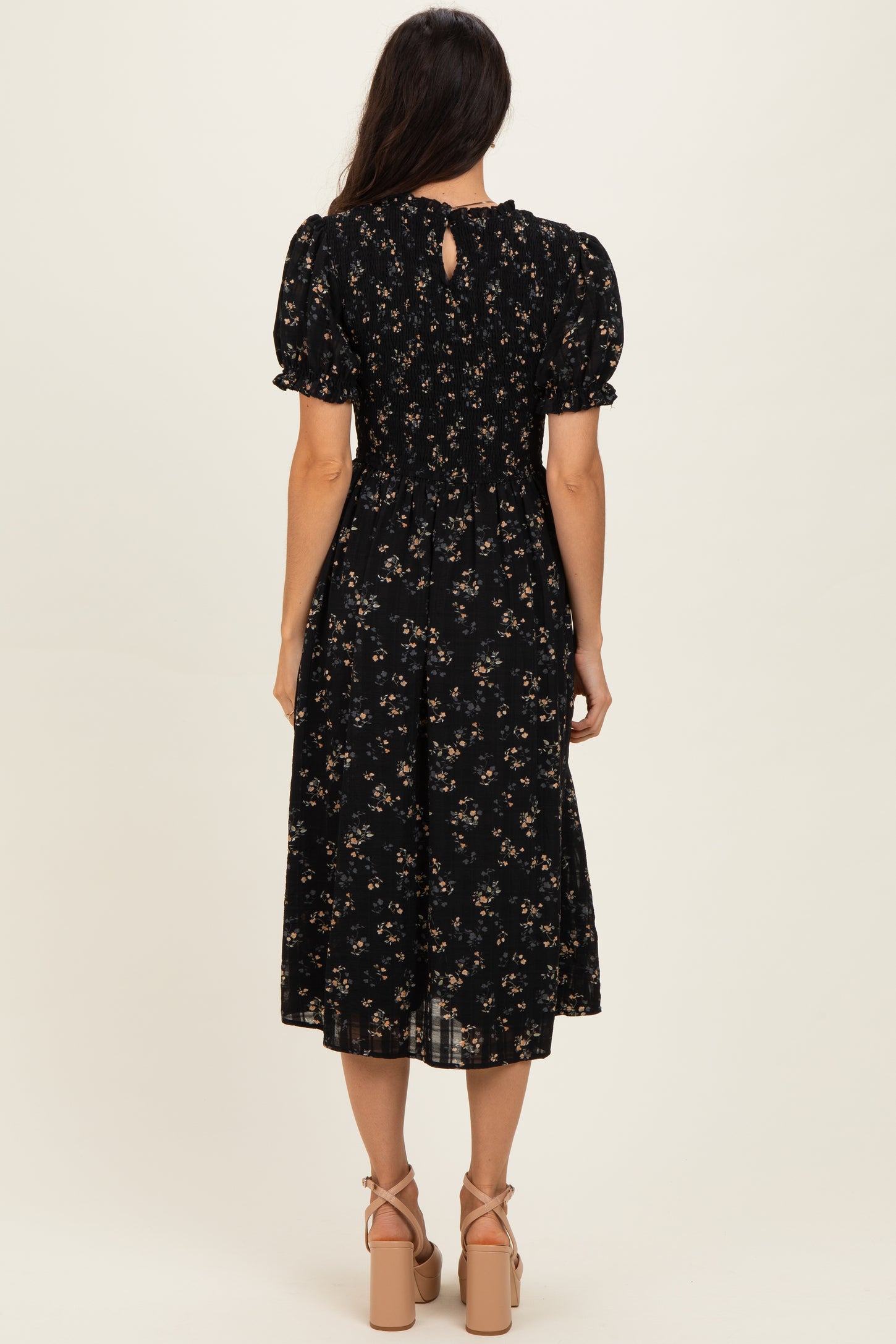 woman wearing a black floral midi dress with puff sleeves and a keyhole detail at the back