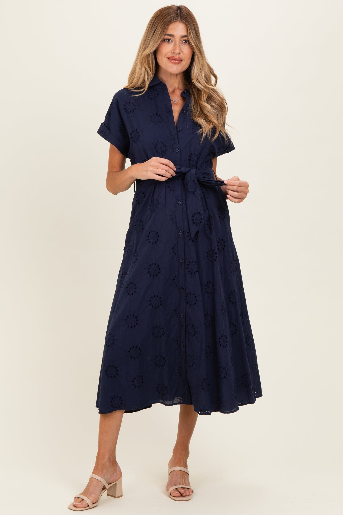 woman wearing a navy blue short sleeve maternity dress with an embroidered floral pattern and a tied waist