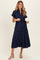woman wearing a navy blue short sleeve maternity dress with an embroidered floral pattern and a tied waist