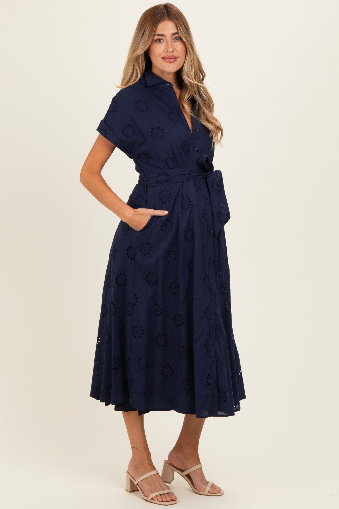 woman wearing a navy blue maternity dress with short sleeves, a tie belt, and floral embroidery details