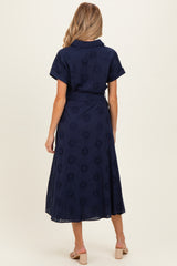 woman wearing a navy blue maternity wrap dress with floral embroidery and short sleeves, view from the back