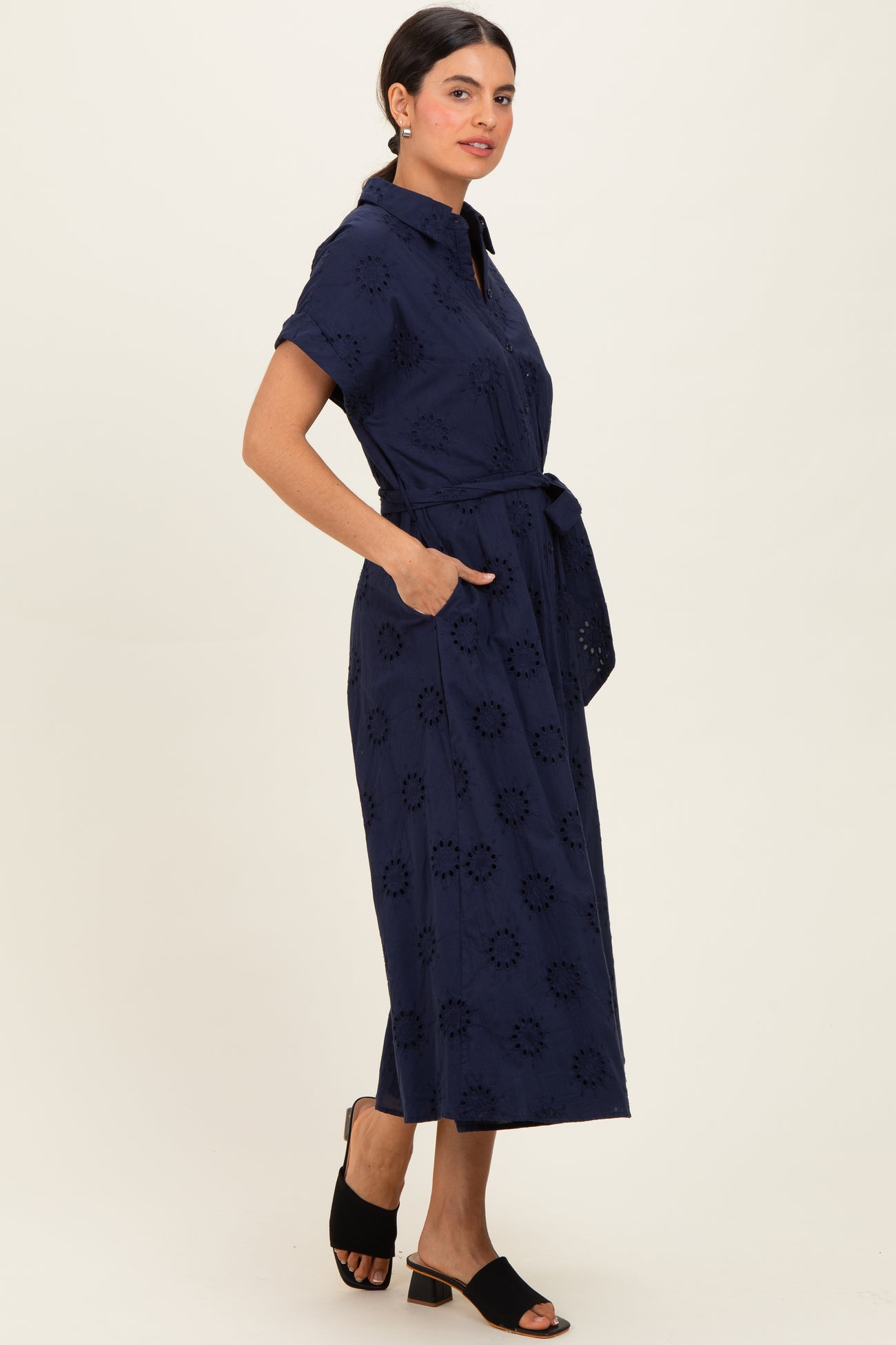 woman wearing a navy blue short sleeve button-up dress with an embroidered floral pattern and a tied waist belt