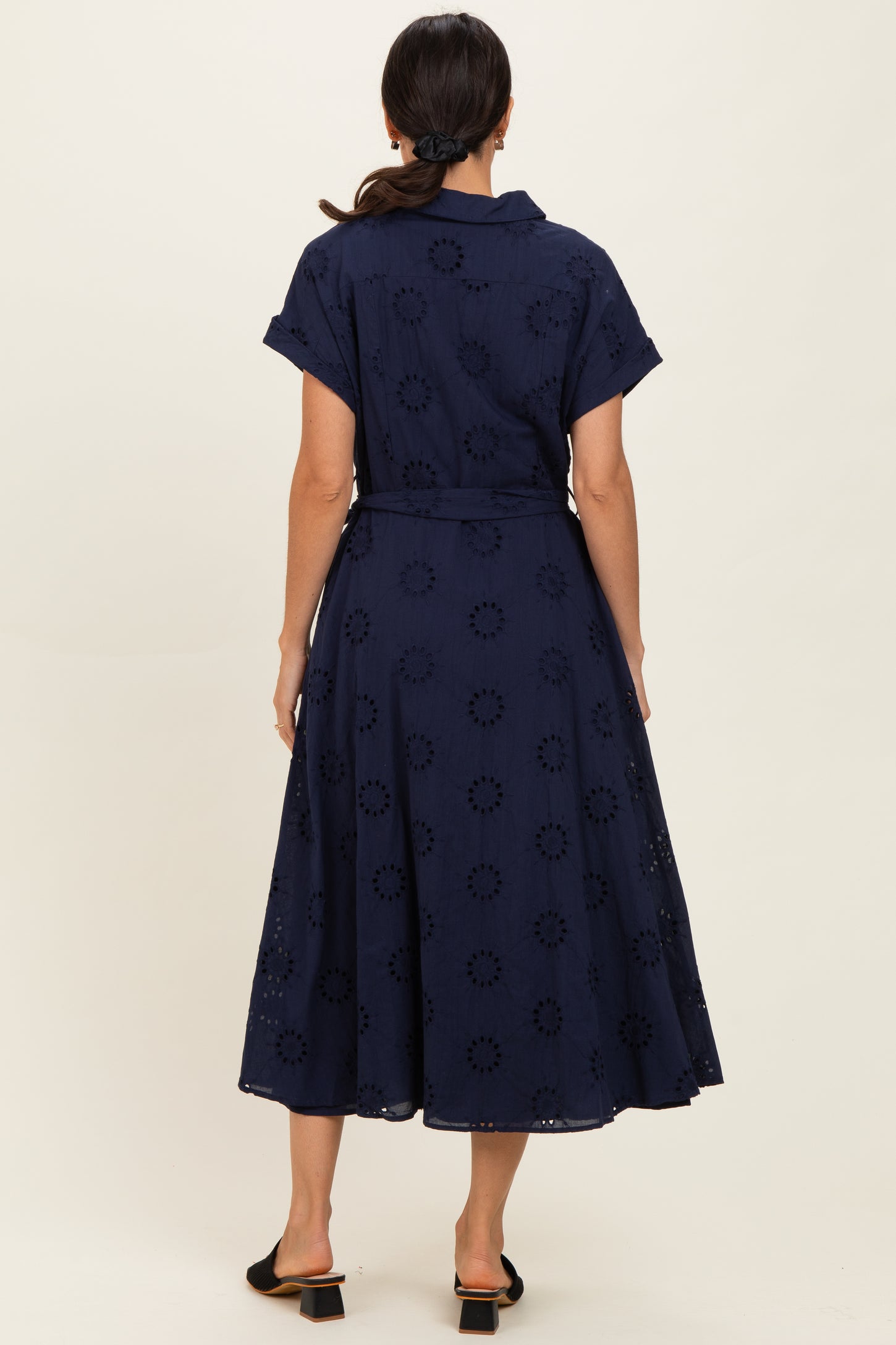 woman wearing a navy blue short sleeve midi dress with a belted waist and floral embroidery details, seen from the back