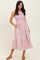 woman wearing a pink sleeveless maxi dress with pockets and a gathered waist, standing on a light background
