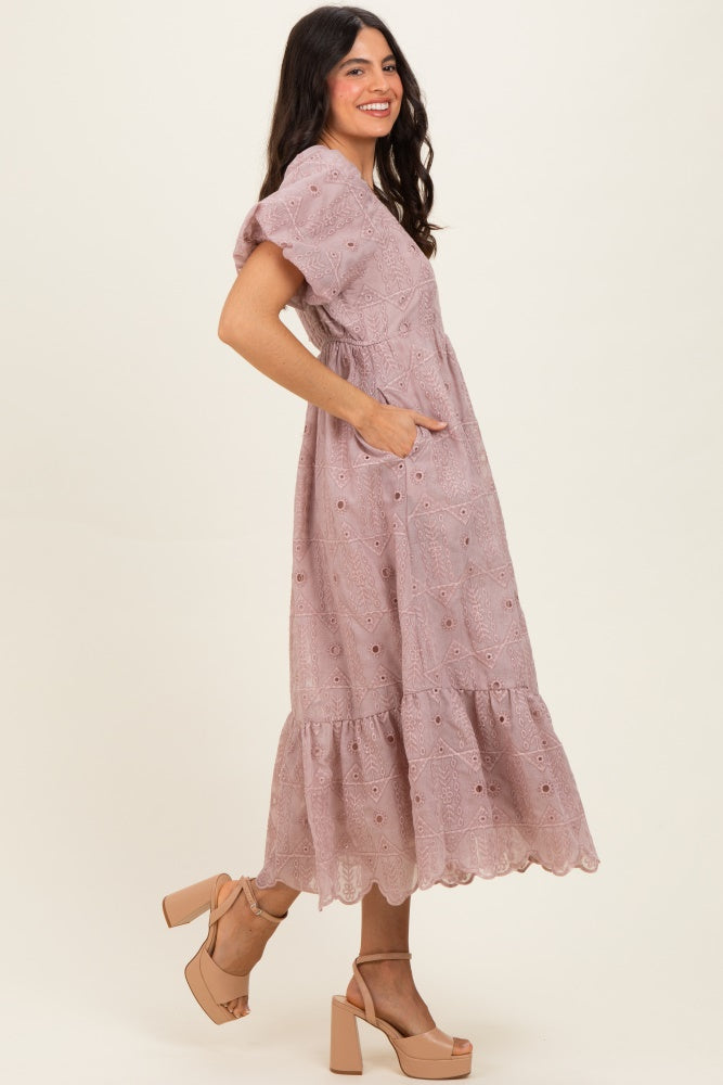 woman wearing a light pink midi dress with embroidery and puff sleeves, showing pockets, paired with block-heeled sandals