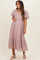 woman wearing a dusty pink embroidered maternity dress with puff sleeves and a ruffle hem, showcasing her baby bump