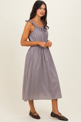 woman wearing a sleeveless gray and white striped midi dress with ruffle details and a tie at the neckline