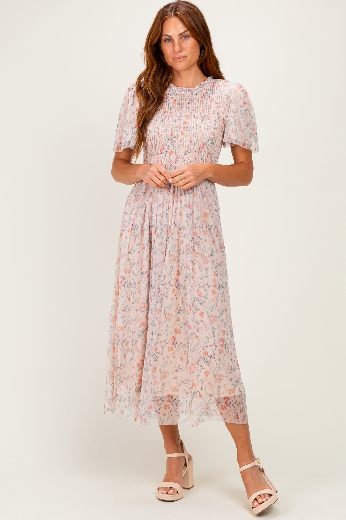 woman wearing a light pink floral midi dress with puff sleeves and a smocked bodice, standing in stylish heels