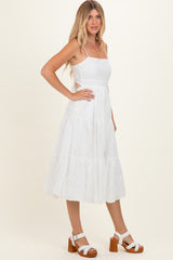 woman wearing a white sleeveless midi dress with tiered detailing and eyelet lace trim, paired with brown block-heeled sandals