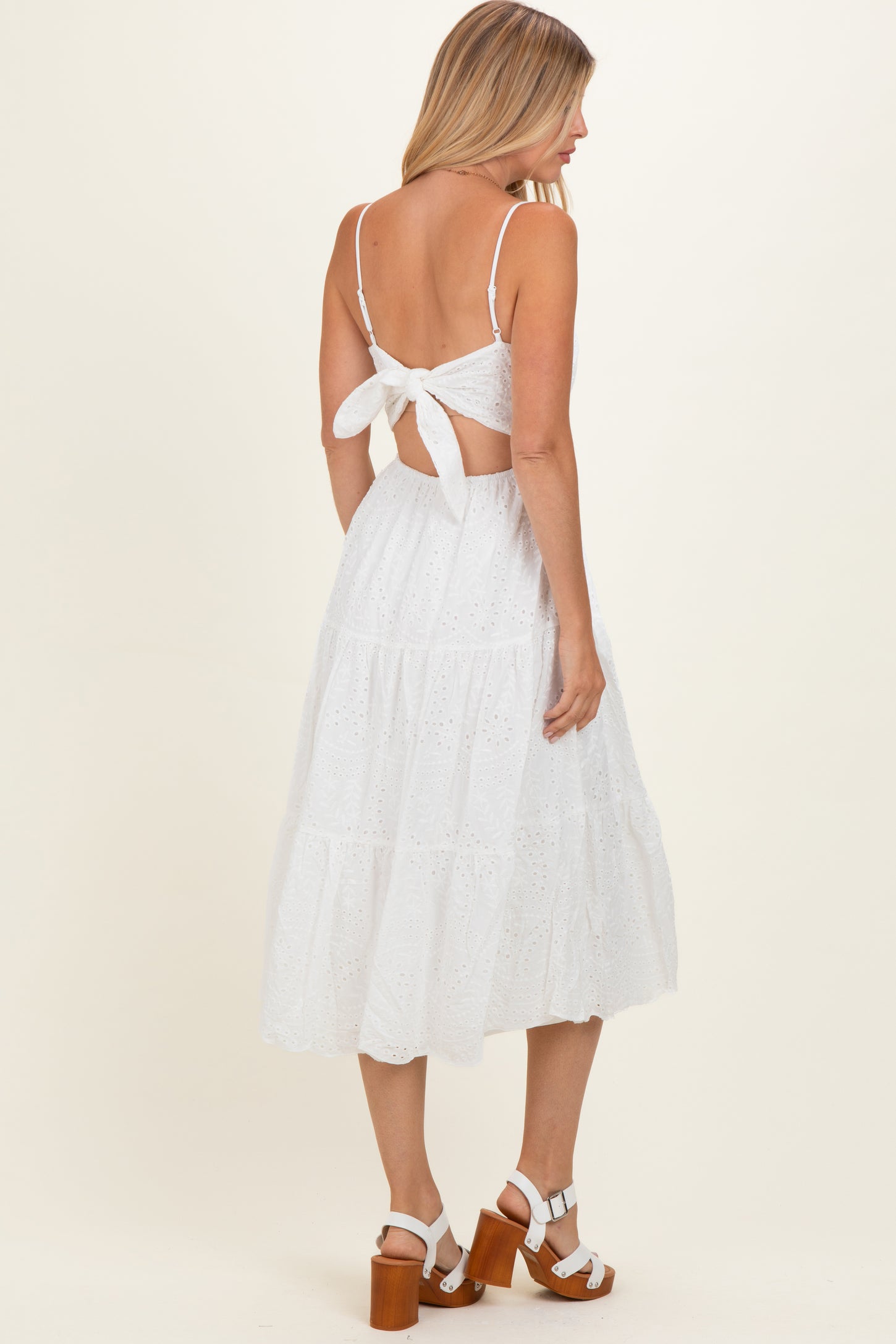 woman wearing a white tiered midi dress with a bow detail on the back and strappy shoulders