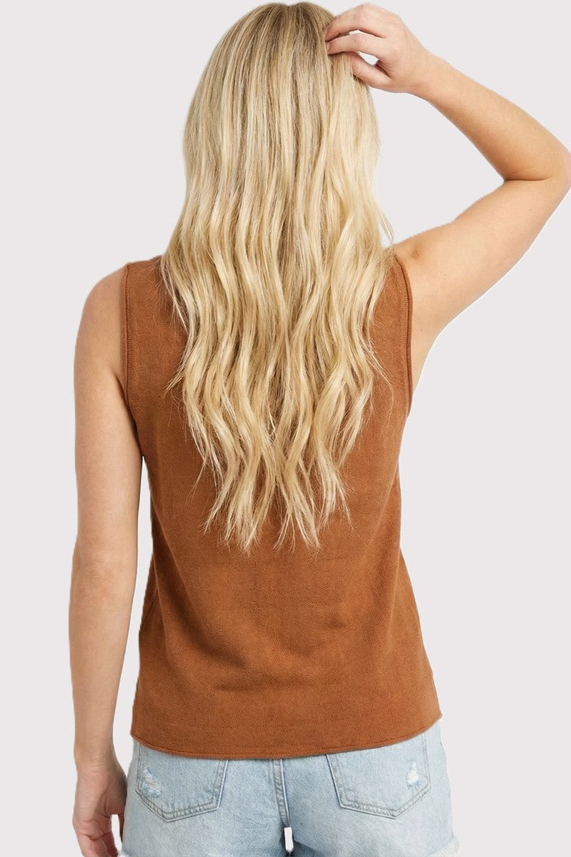 woman wearing a brown sleeveless top and light blue distressed denim shorts, showing her back and long wavy hair