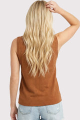 woman wearing a brown sleeveless top and light blue distressed denim shorts, showing her back and long wavy hair