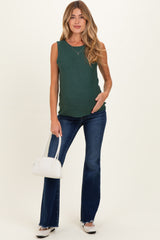 woman wearing a green sleeveless maternity top and blue flared jeans, holding her baby bump with a white handbag
