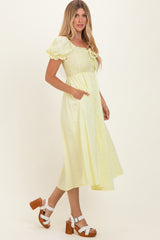 woman wearing a yellow puff sleeve midi dress with a smocked bodice and pockets