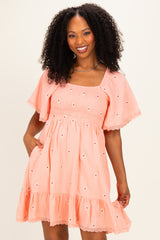 woman wearing a peach short sleeve smocked dress with textured fabric and floral embroidery details