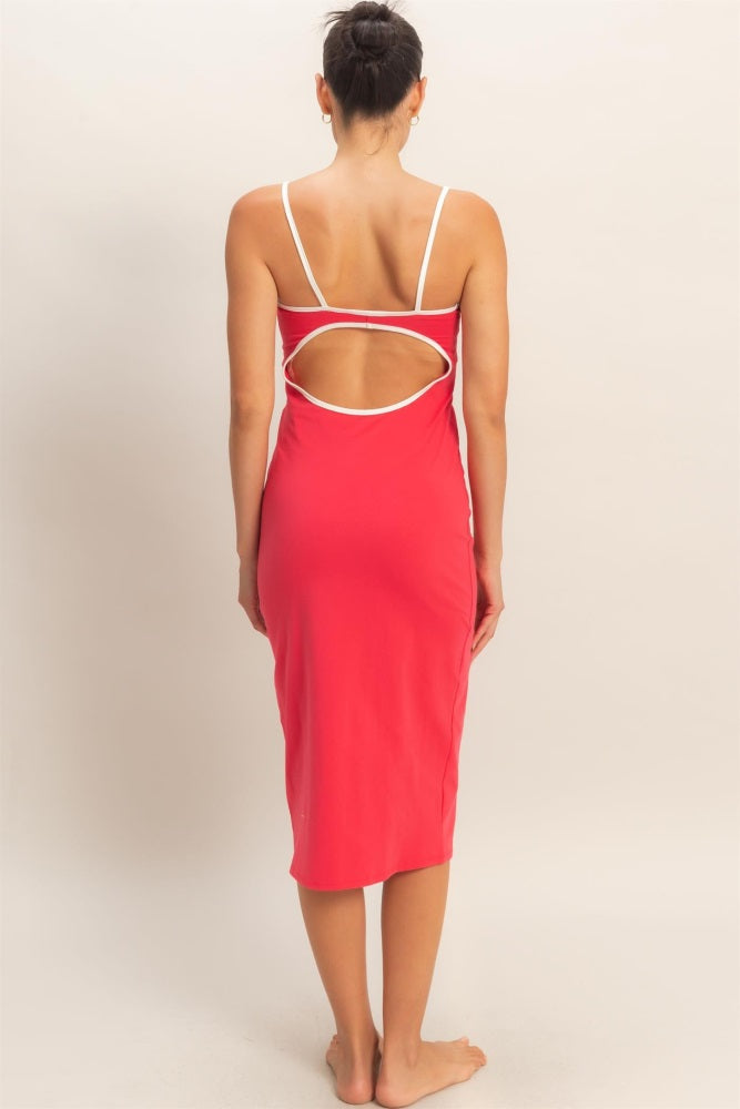 woman wearing a coral midi dress with a white trim and an open back design, standing barefoot