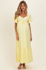 woman wearing a light yellow maternity maxi dress with short flutter sleeves and a gathered bust, showcasing a baby bump