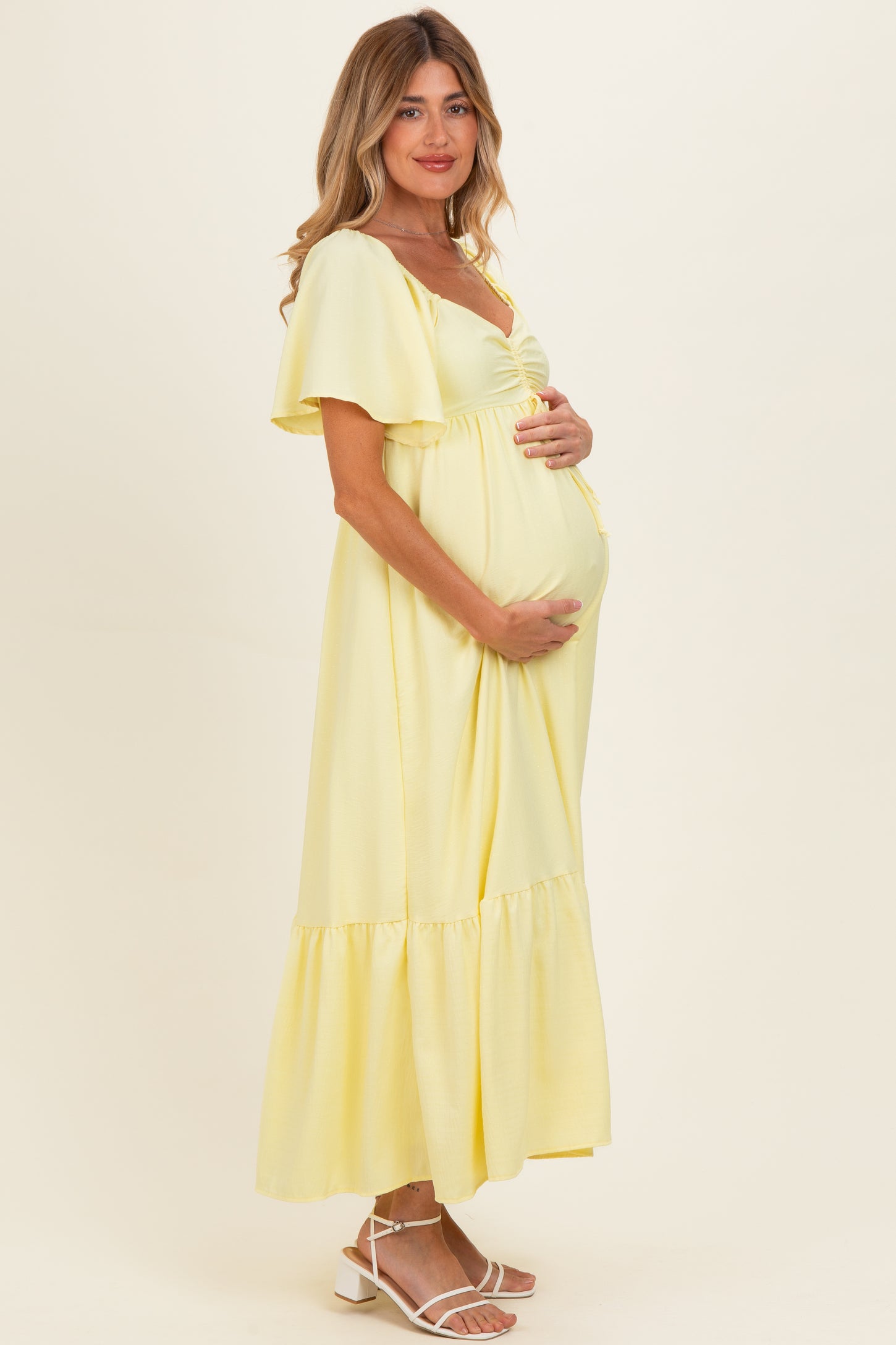 woman wearing a yellow maternity maxi dress with short flutter sleeves and a ruffled hem, holding her baby bump