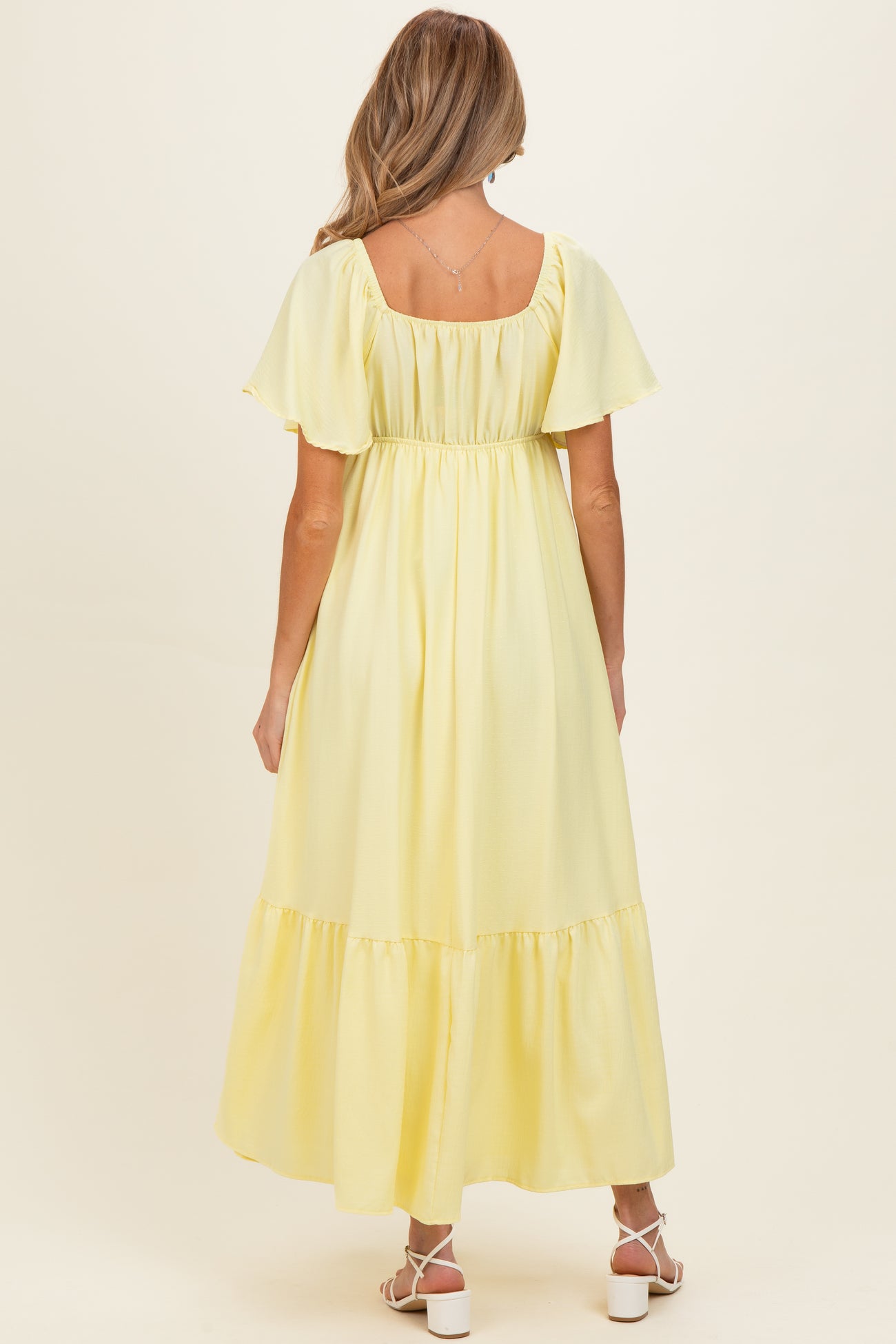 woman wearing a pastel yellow maternity maxi dress with short flutter sleeves and a tiered skirt