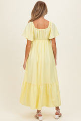 woman wearing a pastel yellow maternity maxi dress with short flutter sleeves and a tiered skirt