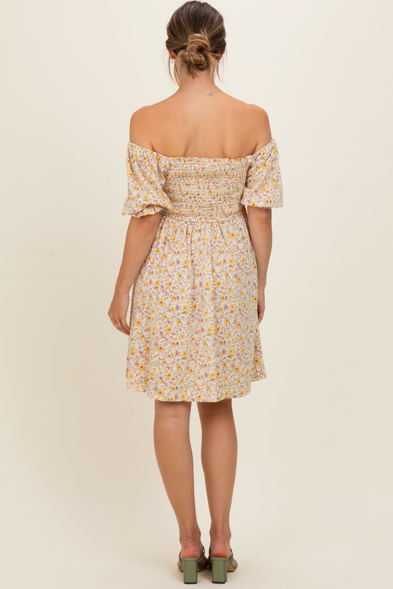 woman wearing a yellow floral off-the-shoulder maternity dress with a fitted bodice and puff sleeves, view from the back