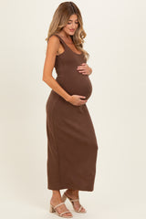 woman wearing a brown sleeveless maternity dress, gently cradling her baby bump