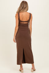 woman wearing a brown sleeveless maternity maxi dress with a back cutout and side slit.