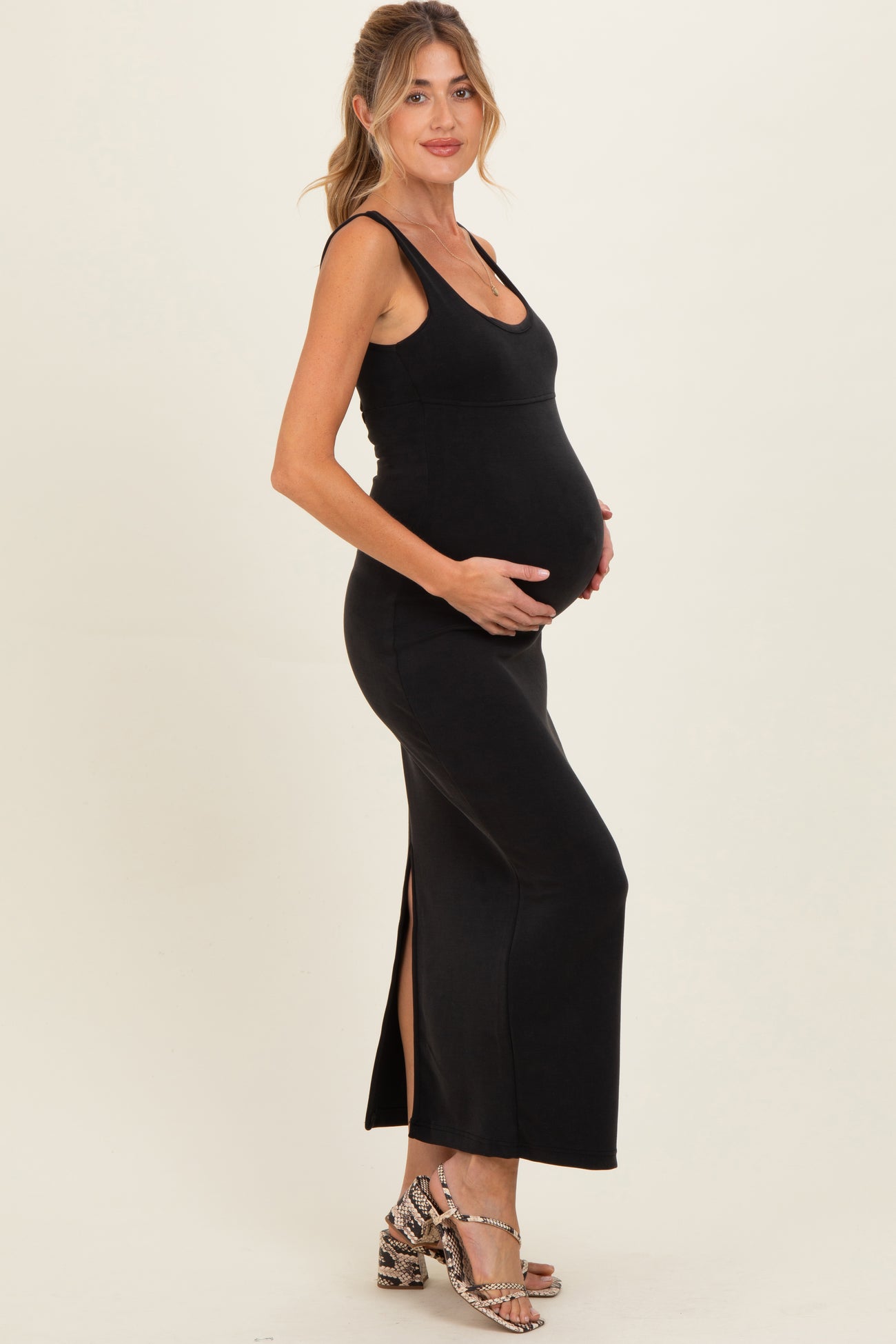 woman wearing a black sleeveless maternity maxi dress, showcasing her baby bump, with side slits at the hem