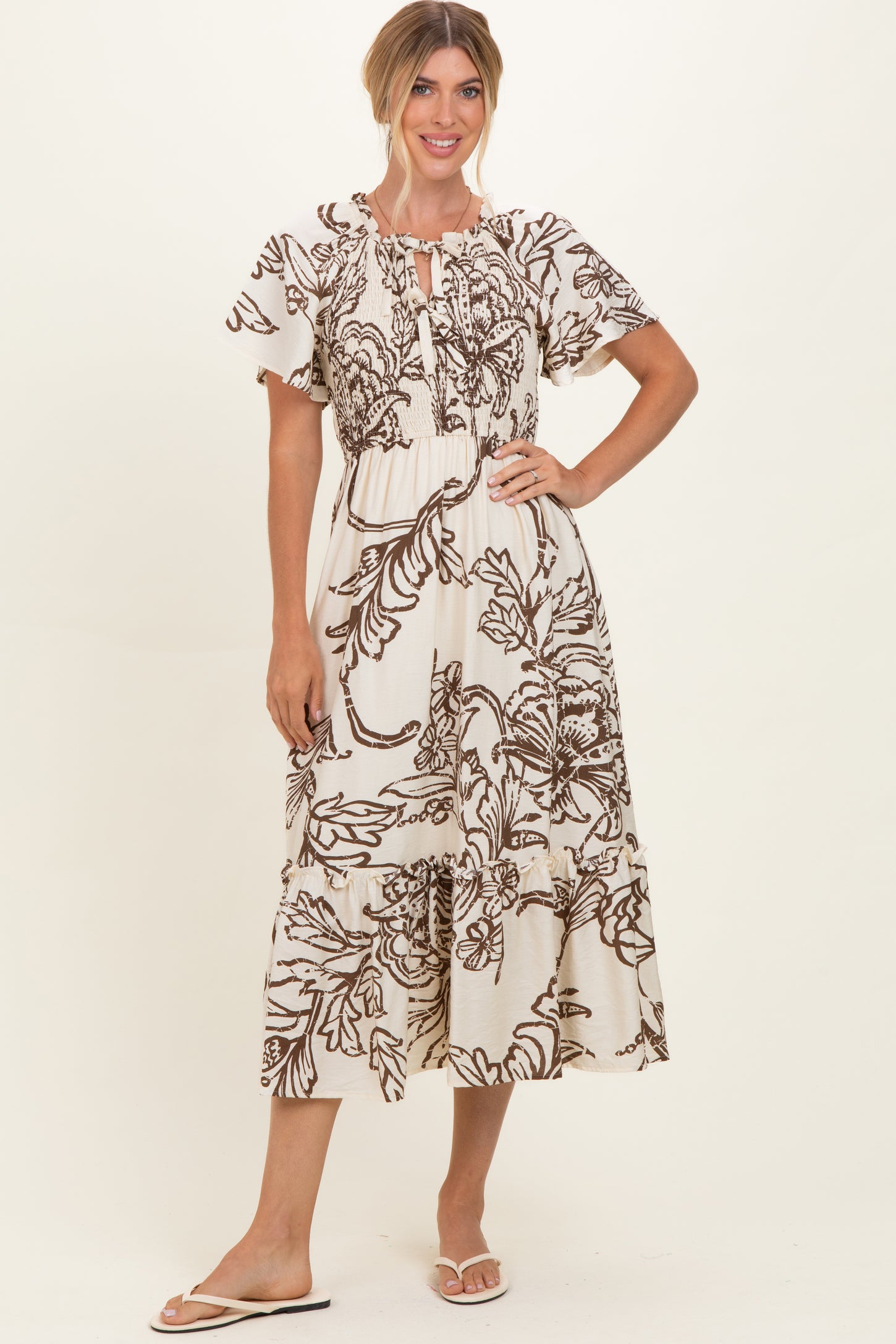 woman wearing a cream maxi dress with brown floral print and puff sleeves, standing with her hand on her hip