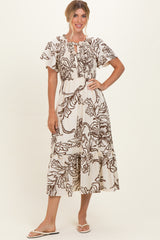 woman wearing a cream maxi dress with brown floral print and puff sleeves, standing with her hand on her hip