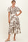 woman wearing a cream maxi dress with brown floral print and puff sleeves, standing with her hand on her hip