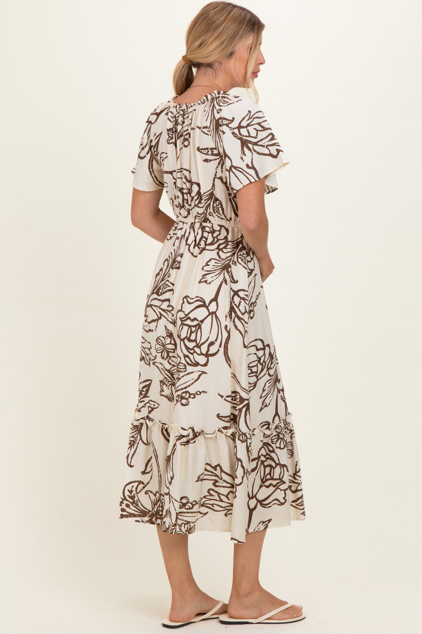 woman wearing a beige floral print maxi dress with short sleeves and a fitted waist, standing sideways