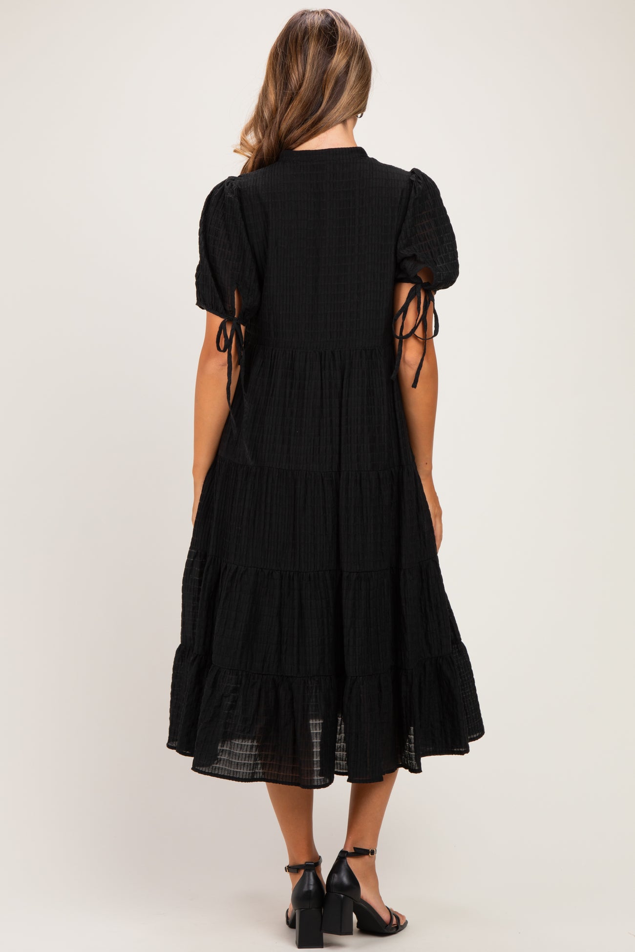 woman wearing a black tiered maternity dress with puff sleeves and tie details at the arms