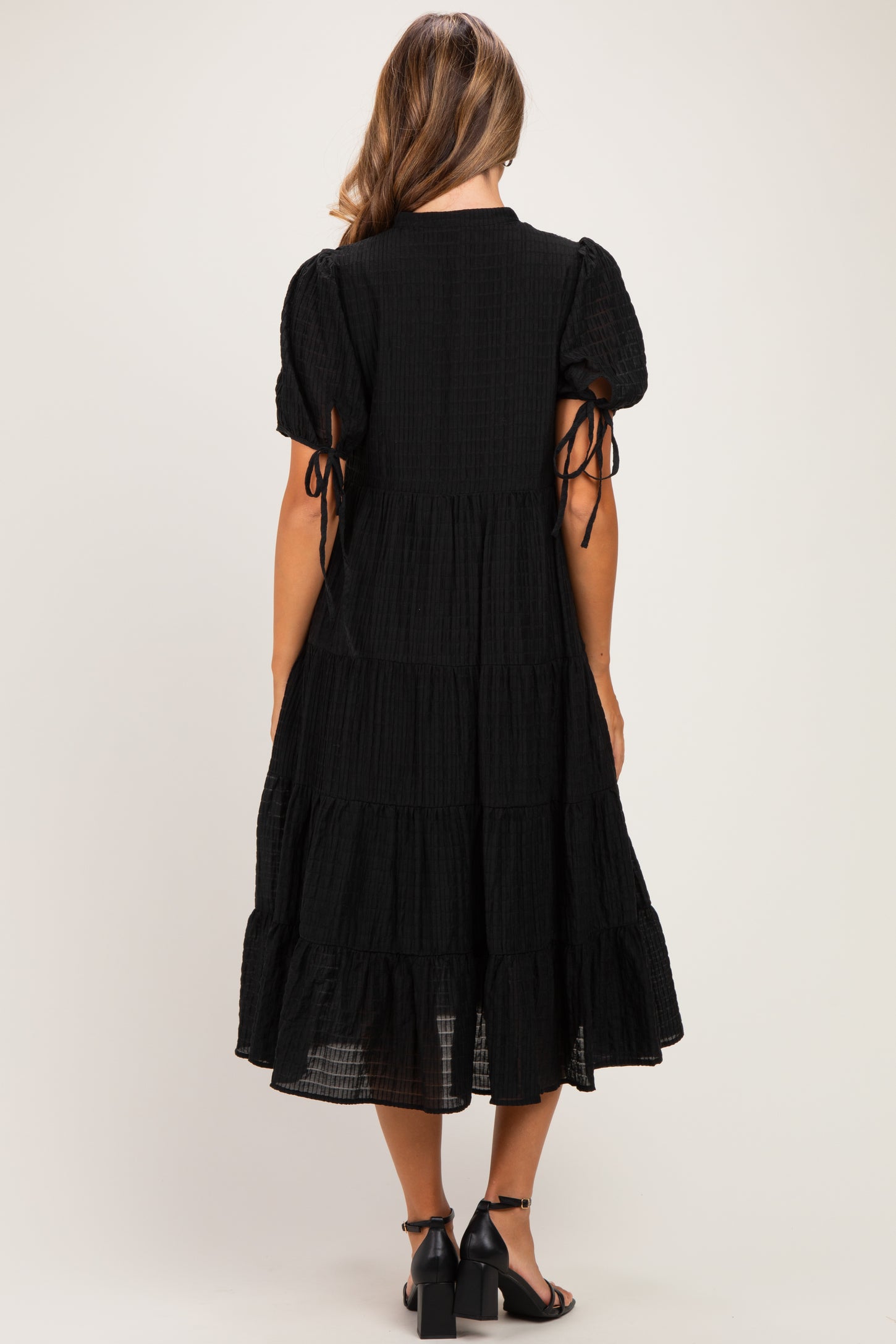 woman wearing a black tiered maternity dress with puff sleeves and tie details at the arms