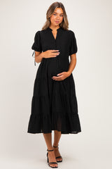 woman wearing a black maternity dress with short puff sleeves and a tiered skirt, holding her baby bump